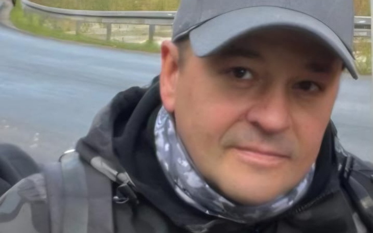 Mężczyzna w czapce, uśmiechnięty, na tle drogi.