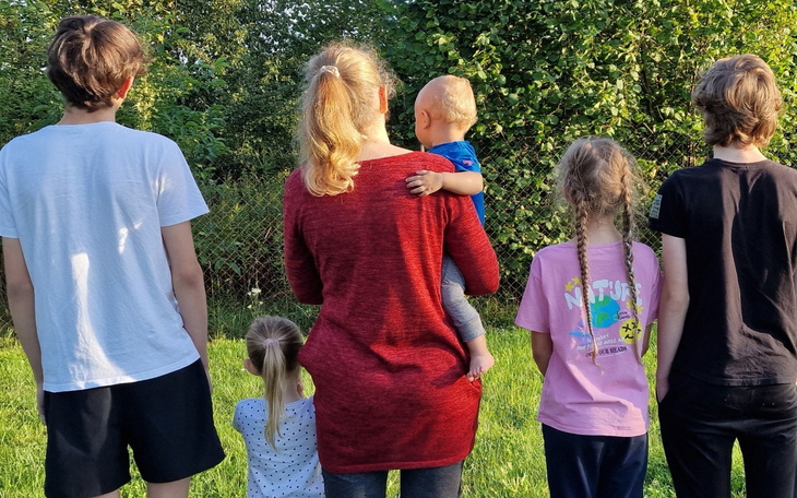 Grupa dzieci i dorosłych stoi tyłem, patrząc w dal.