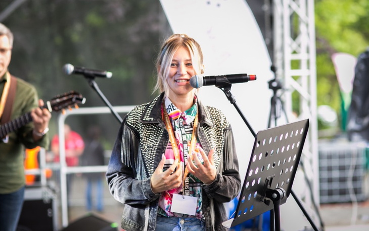 Młoda kobieta przemawiająca na scenie, z mikrofonem w ręku.