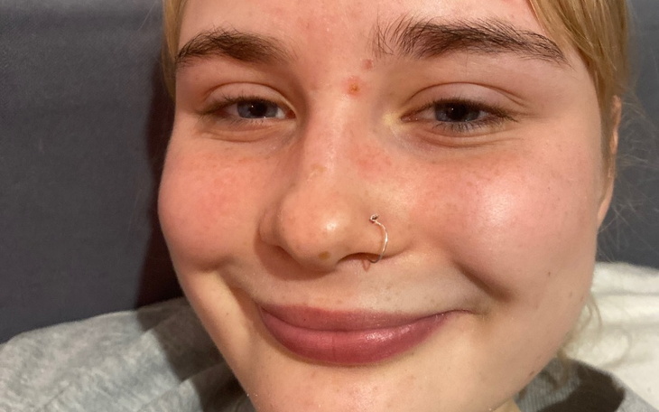 Młoda kobieta z kolczykiem w nosie, uśmiechająca się do obiektywu.