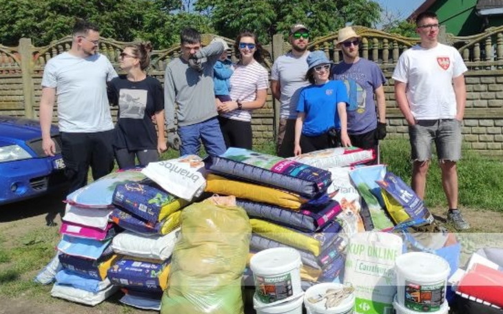 Grupa ludzi z darami dla zwierząt, w tle stos worków z karmą.