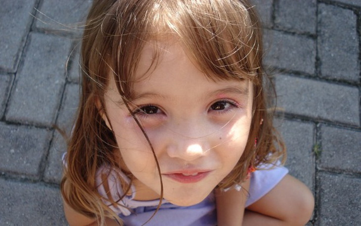 Uśmiechnięta dziewczynka na chodniku, patrząca w obiektyw.