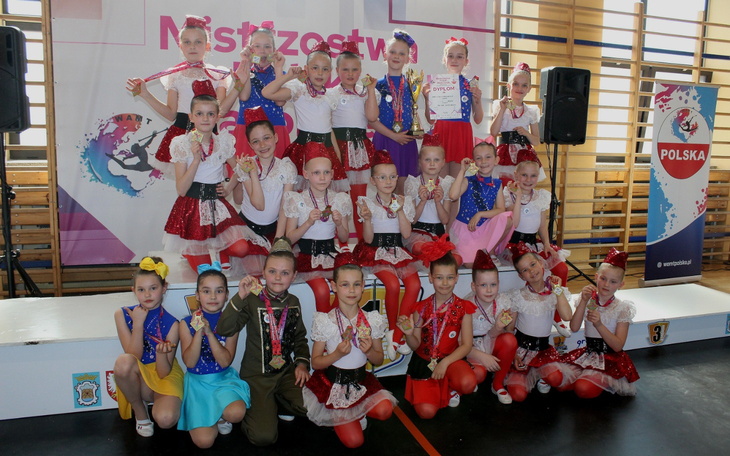 Grupa dzieci w strojach tanecznych z medalami.