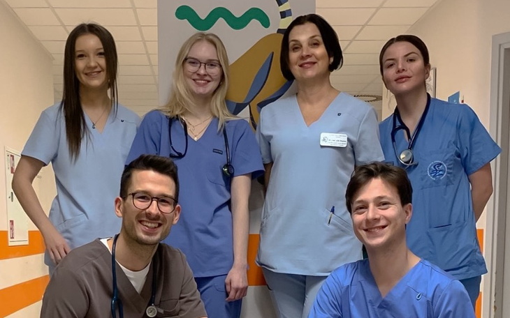 Zespół medyczny w niebieskich uniformach, uśmiechnięty w szpitalnym korytarzu.