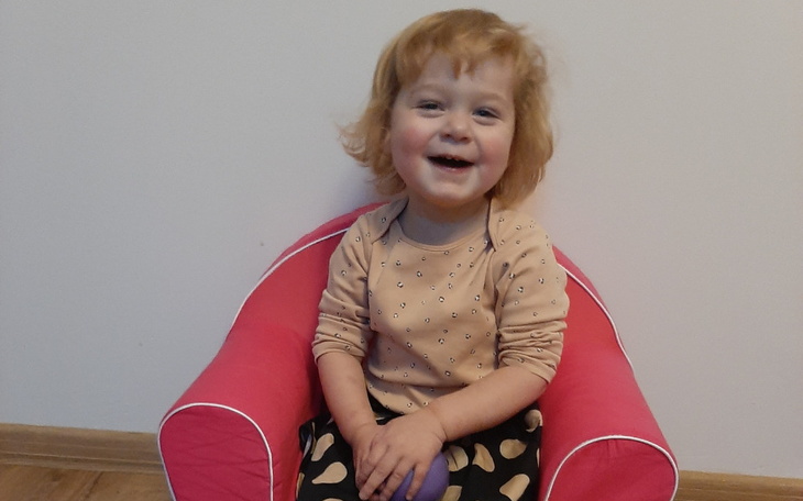 Uśmiechnięta dziewczynka siedząca na różowym foteliku.