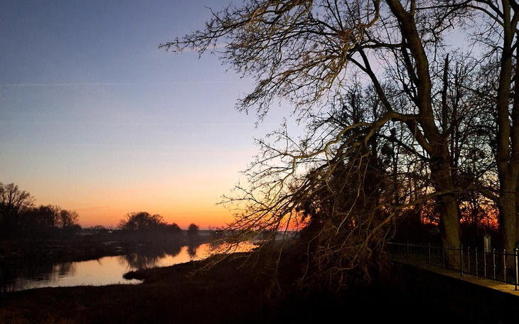 Zachód słońca nad rzeką, z drzewami w tle.