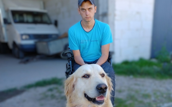 Mężczyzna na wózku inwalidzkim z psem w tle.