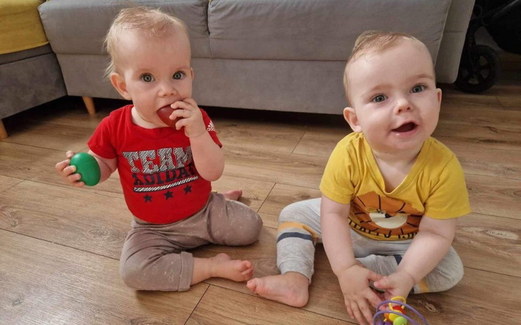 Dwa uśmiechnięte maluchy bawią się w domu, trzymając kolorowe zabawki.