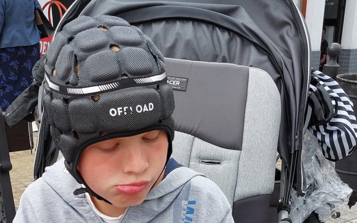 Chłopiec w kasku ochronnym, siedzący w wózku dziecięcym.