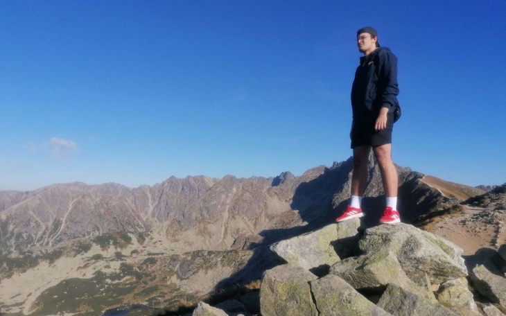 Mężczyzna stojący na szczycie góry, z widokiem na krajobraz.