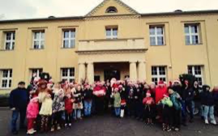 Grupa ludzi w czapkach Mikołaja przed budynkiem.