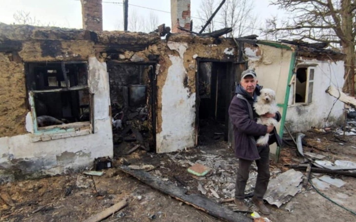 Mężczyzna trzymający psa przed zniszczonym domem.