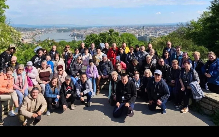 Grupa ludzi na wzgórzu z widokiem na miasto i rzekę w tle.