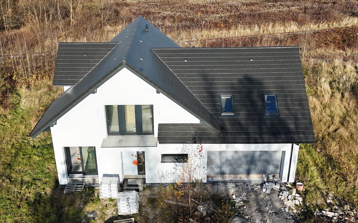 Nowoczesny dom z dużymi oknami, otoczony naturą.