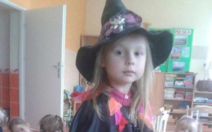 Dziewczynka w czarnej pelerynie i kapeluszu, wygląda jak czarownica.