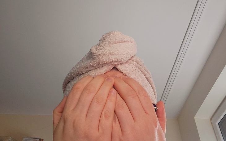 Osoba z ręcznikiem na głowie, zakrywająca twarz dłońmi.