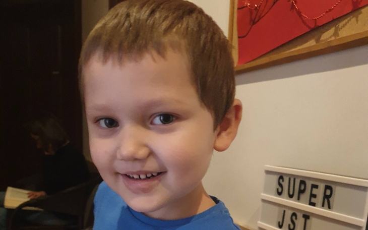 Chłopiec z uśmiechem, w niebieskiej koszulce, w przytulnym wnętrzu.