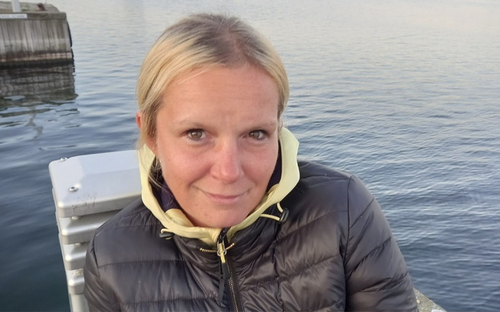 Kobieta w kurtce, uśmiechająca się na tle wody.