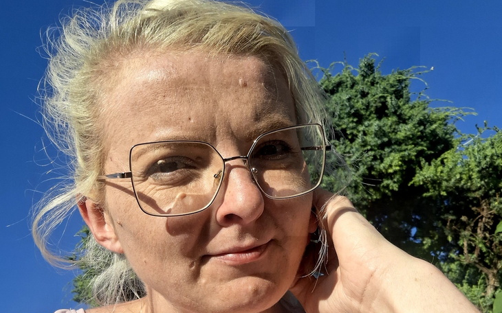 Kobieta z okularami, uśmiechająca się w słonecznym otoczeniu.