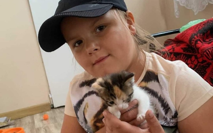 Dziewczynka w czapce trzyma małe kocię na rękach.