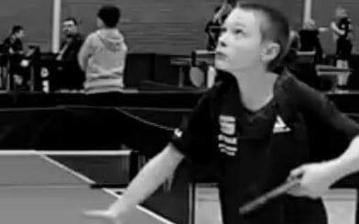 Młody gracz tenisa stołowego w trakcie meczu, skupiony na grze.