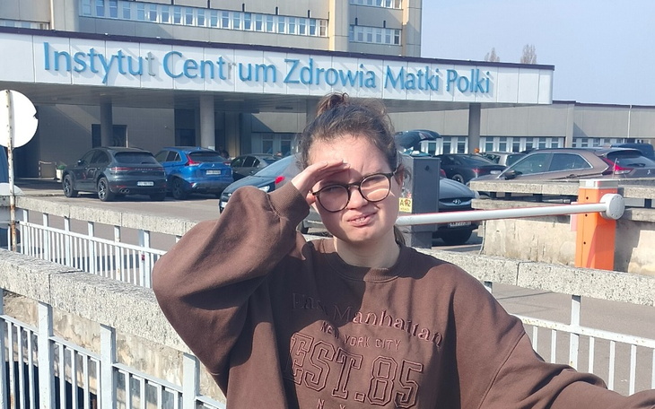 Młoda dziewczyna w okularach stoi przed Instytutem Zdrowia Matki Polki.