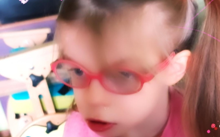 Dziewczynka w różowych okularach, uśmiechająca się do kamery.