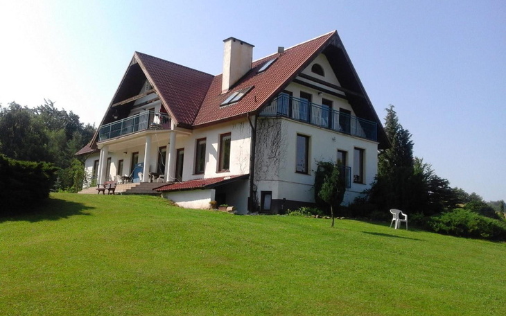 Widok na duży dom z ogrodem w słoneczny dzień.