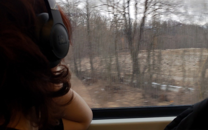 Osoba w słuchawkach patrząca przez okno pociągu na las.