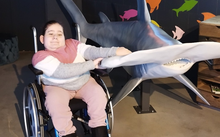 Dziecko na wózku inwalidzkim, trzymające rekina z plastiku.