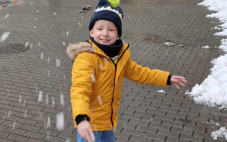 Chłopiec w żółtej kurtce bawi się w śniegu.