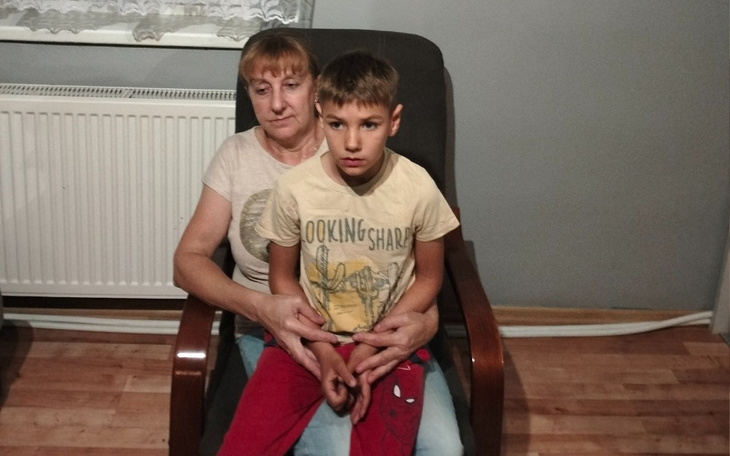 Kobieta trzymająca chłopca na kolanach, oboje wpatrzeni w obiektyw.