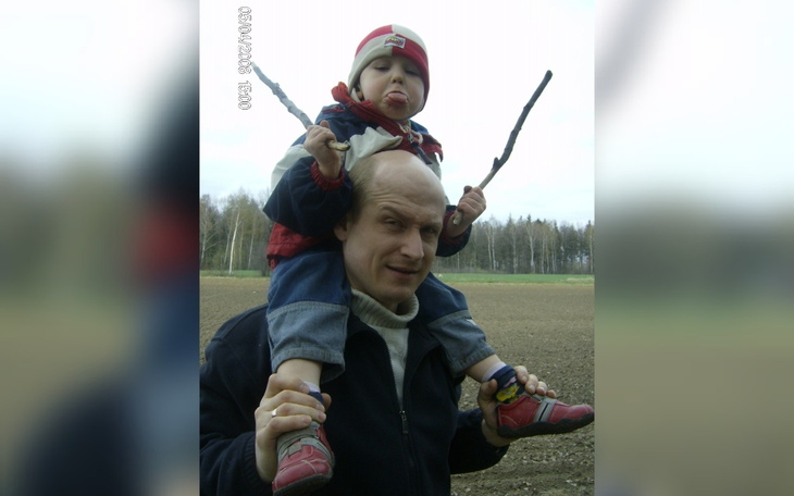 Dziecko na plecach ojca, trzymające patyki i robiące miny.