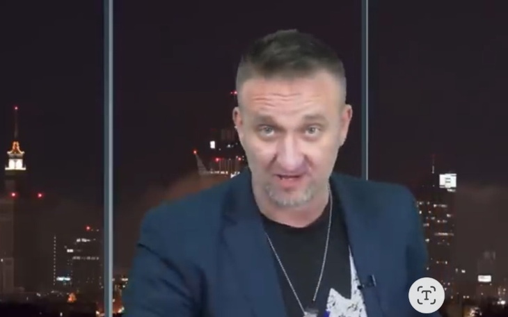 Mężczyzna w garniturze, przemawiający na tle nocnego miasta.