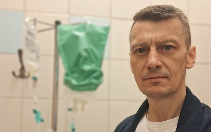 Mężczyzna w szpitalu, z kroplówką w tle.