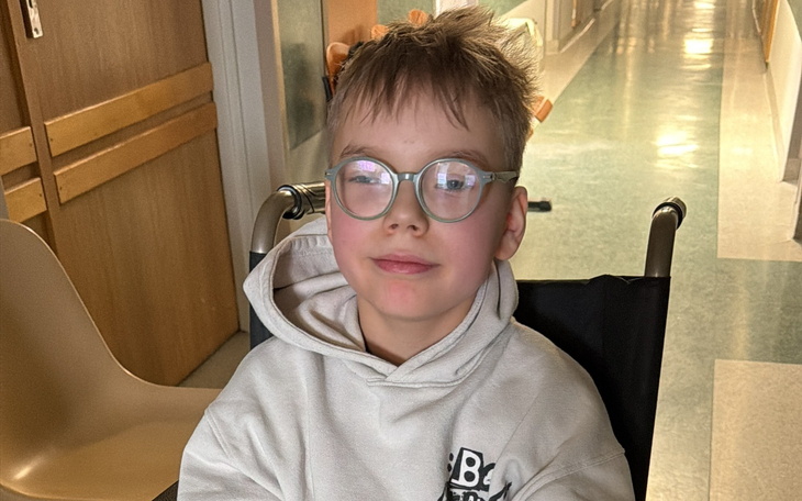 Chłopiec w wózku inwalidzkim, uśmiechnięty i z okularami.