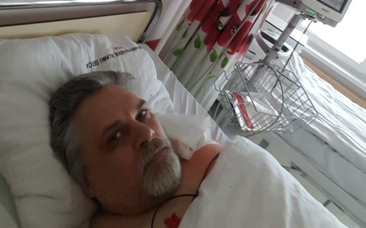 Mężczyzna leżący w szpitalnym łóżku, z poważnym wyrazem twarzy.