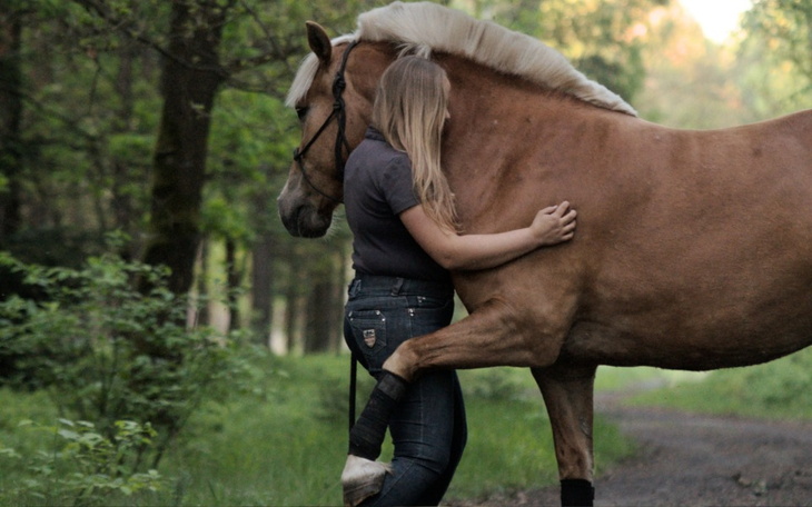 Kobieta przytulająca konia w lesie, w otoczeniu zieleni.
