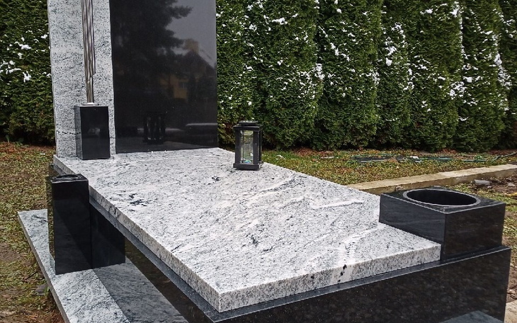 Pomnik z lampionem i czarnym pojemnikiem.