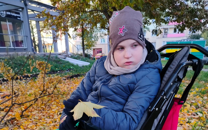 Chłopiec na wózku, trzymający liść w parku.