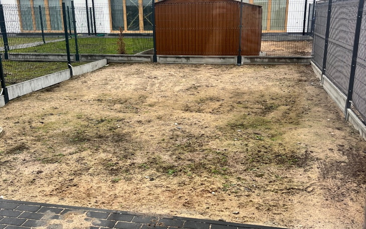 Pusty teren z ogrodzeniem i budynkiem w tle.