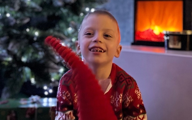 Chłopiec w swetrze świątecznym, uśmiechający się z zabawką.