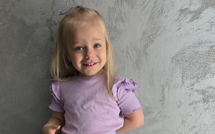 Mała dziewczynka uśmiechająca się w fioletowej bluzce.