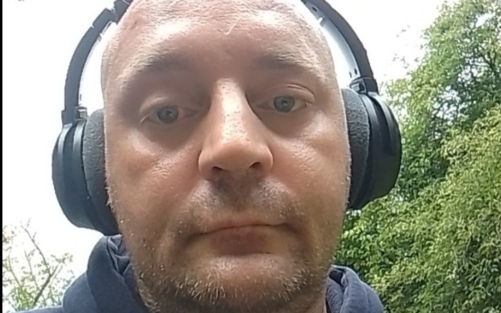 Mężczyzna w słuchawkach, spacerujący w zielonym otoczeniu.