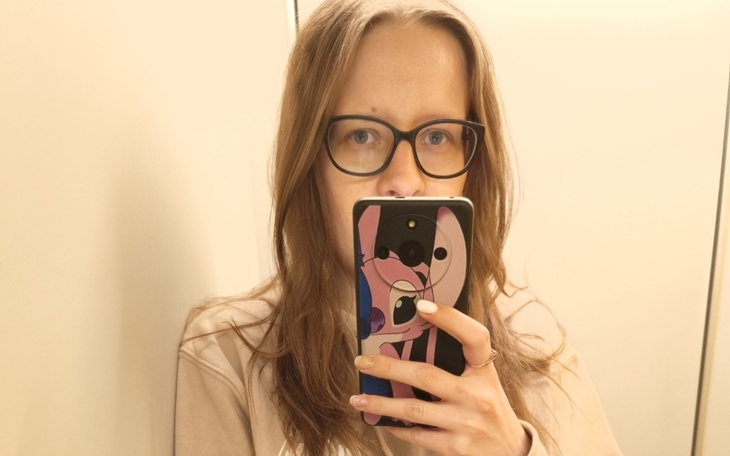 Kobieta z okularami, trzymająca telefon z odbiciem w lustrze.