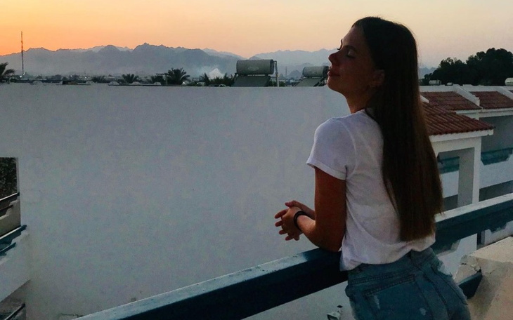 Kobieta na balkonie, podziwiająca zachód słońca w górach.