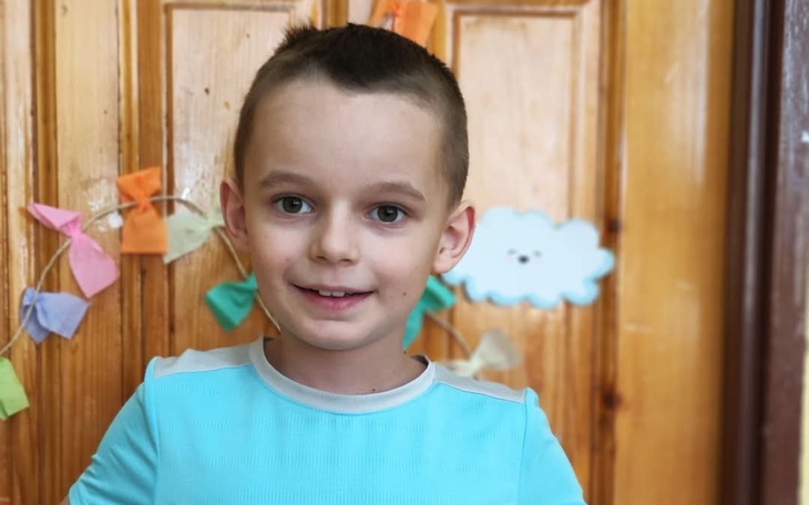 Chłopiec uśmiechający się na tle drewnianych drzwi.