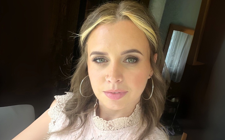 Portret kobiety z uśmiechem, w jasnej bluzce, w naturalnym świetle.