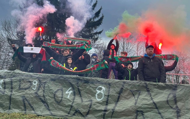 Grupa ludzi z flagami i racami na wzgórzu.