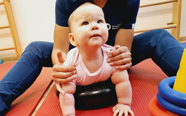 Dziecko w trakcie ćwiczeń, trzymane przez dorosłego.